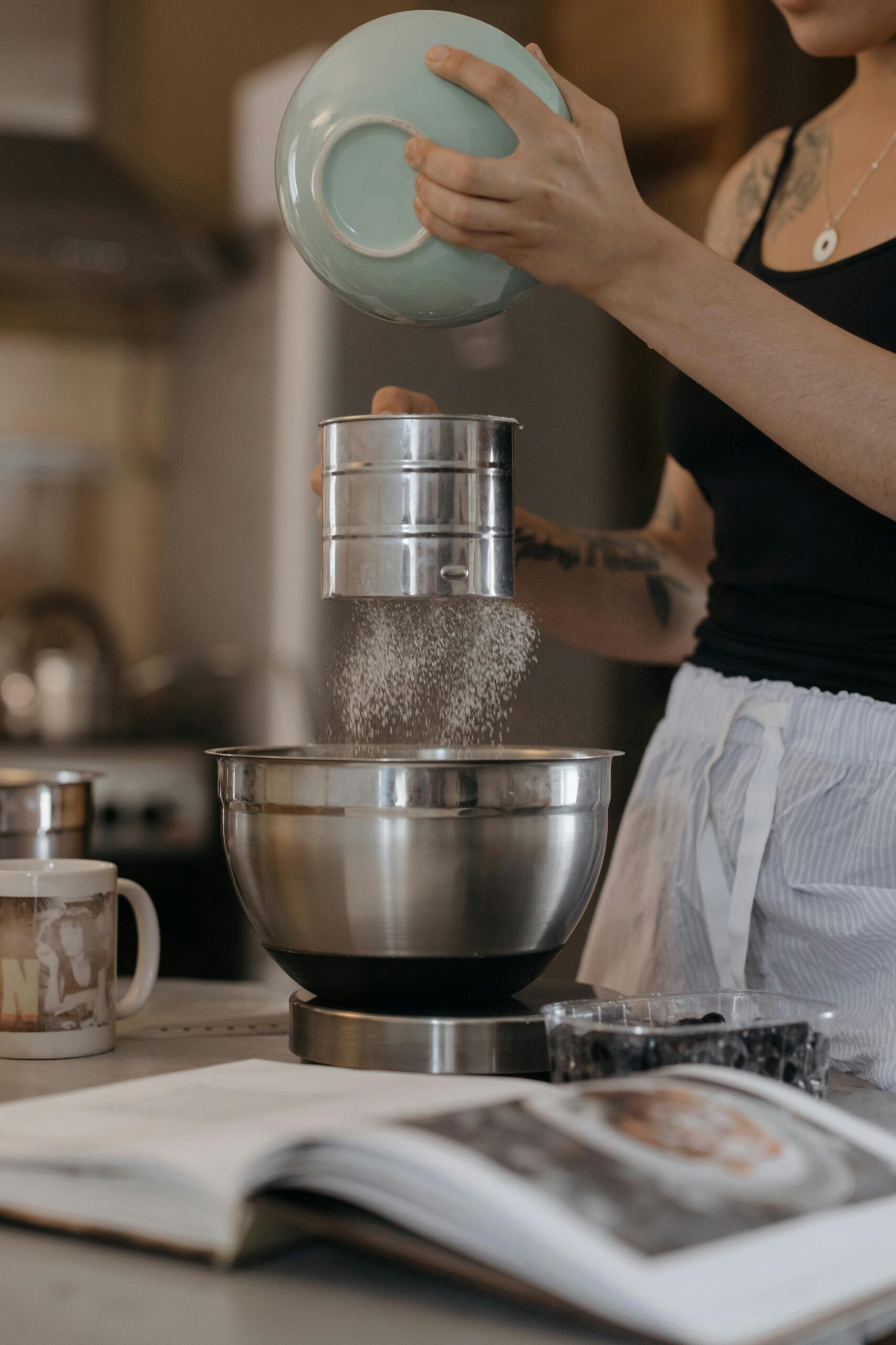 Person sifting flour into a metal mixing bowl while baking in a home kitchen